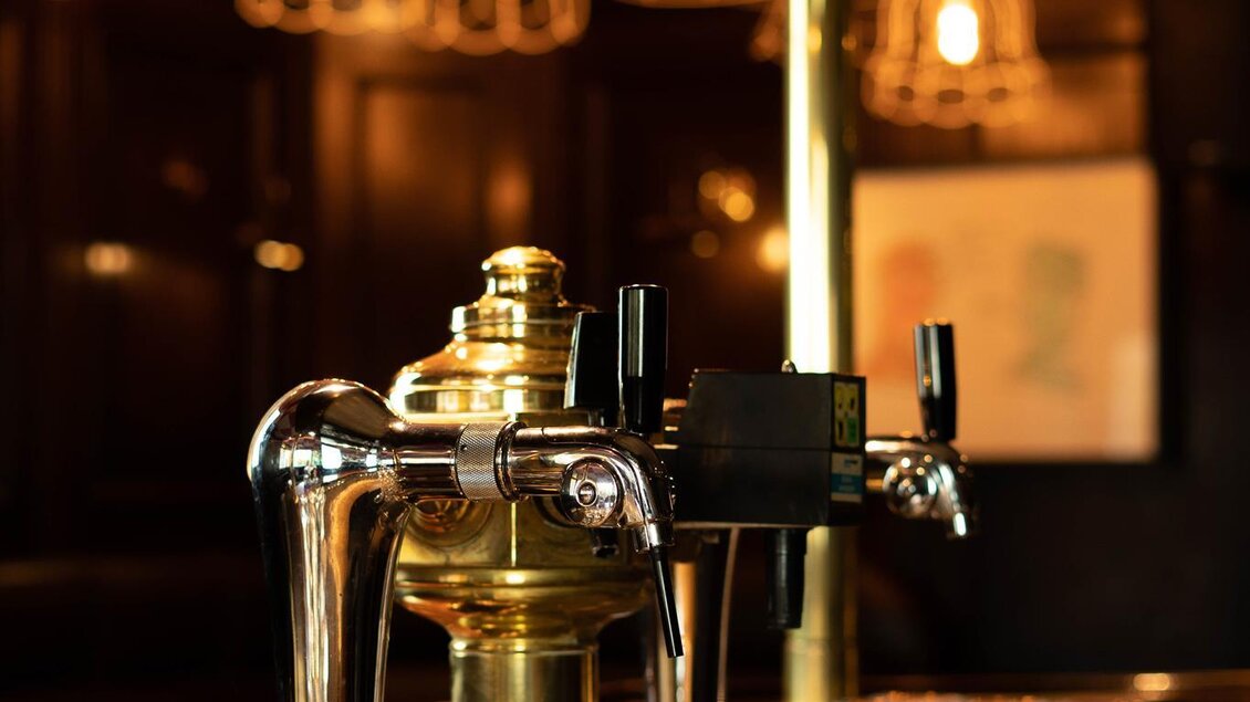 Eine stilvolle Bar mit einem glänzenden Zapfhahn und transparenten Gläsern. Warmes Licht schafft eine einladende Atmosphäre. | © Cafe Beisl