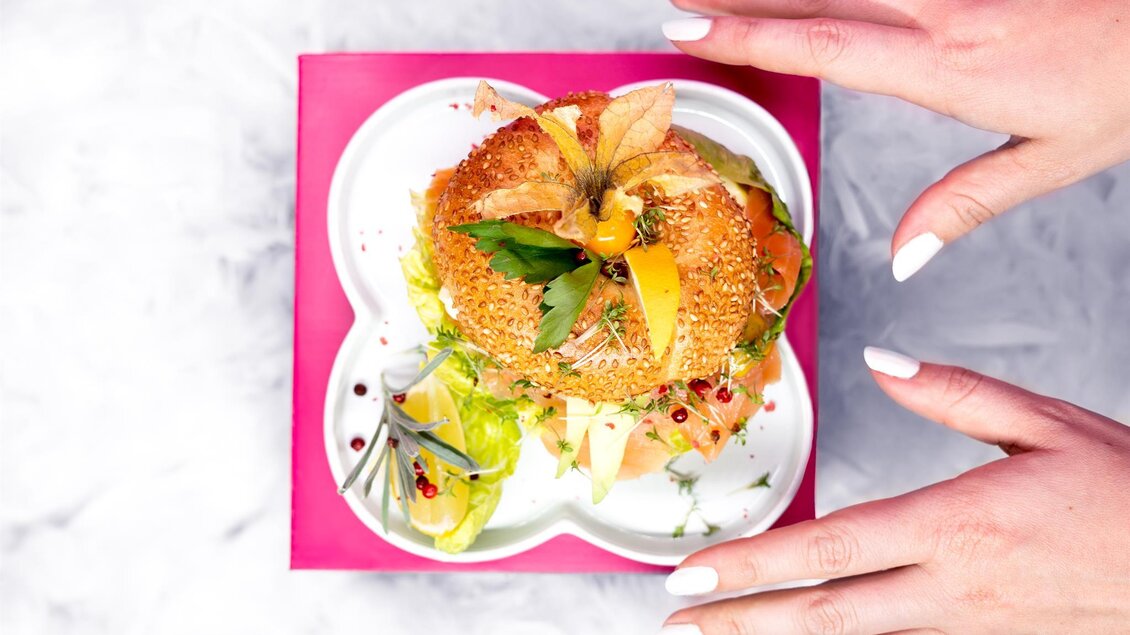 Ein hübsch angerichtetes Gericht auf einem bunten Teller, umgeben von frischen Zutaten. Die Hände einer Person sind bereit, das Essen zu genießen. | © Cafe Beisl