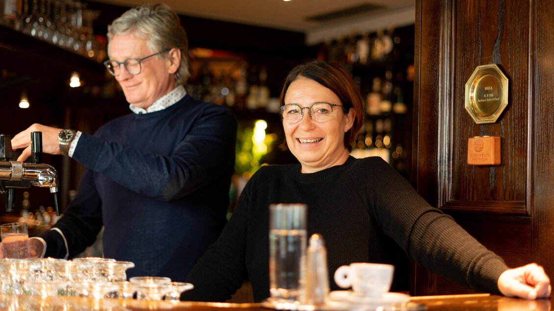 Ein gemütlicher Barbereich mit zwei Bartendern. Der Mann zapft Bier und die Frau lächelt freundlich. | © Cafe Beisl