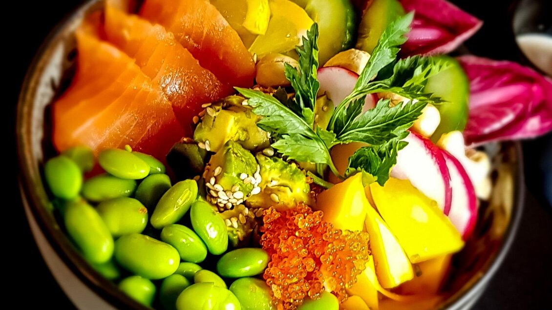 Eine bunte Schüssel mit frischem Sushi, Edamame, Avocado und verschiedenen Gemüsesorten. Die Mischung wird durch Rote-Bete-Blätter und Limettenstücken ergänzt. | © Cafe Beisl