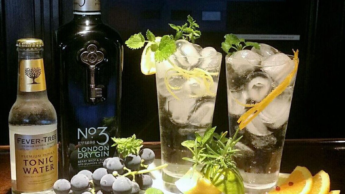 Zwei Gläser mit einem erfrischenden Cocktail aus Gin, Tonic Water und frischen Zutaten. Neben den Cocktails liegen Trauben, Zitronenscheiben und Minze auf einem Holzbrett. | © Café Beisl Feldbach