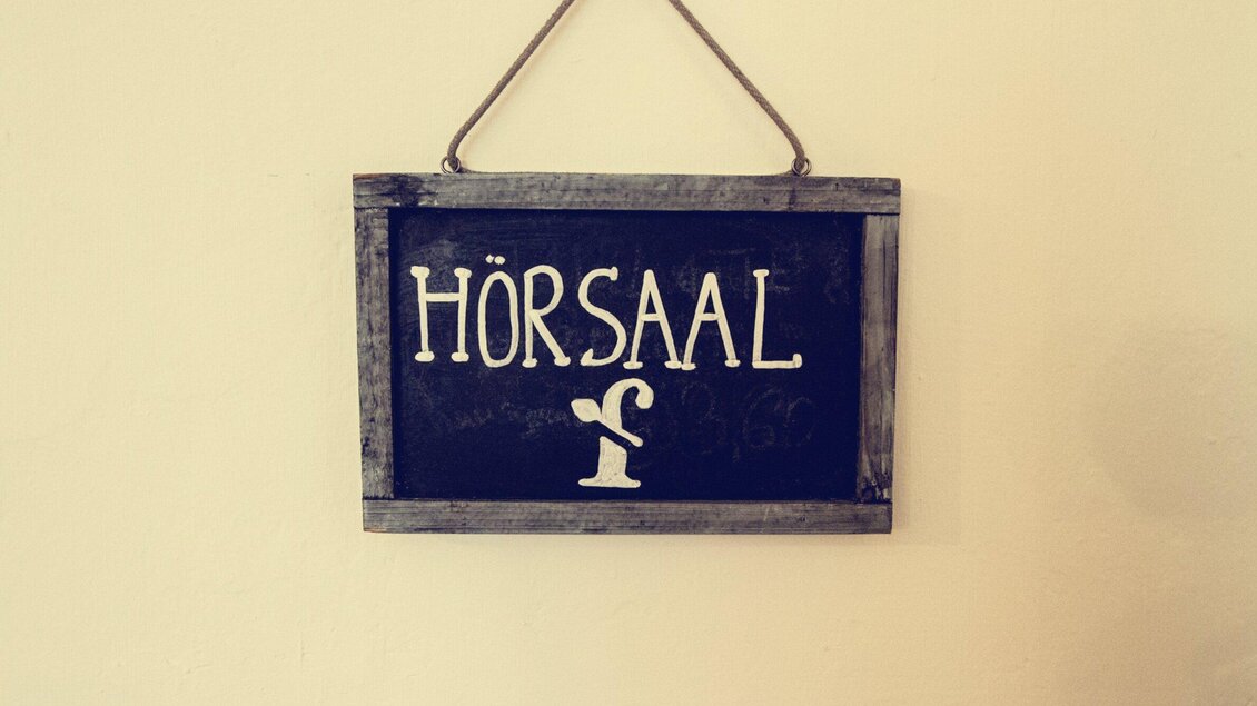 Ein Schild mit der Aufschrift "Hörsaal". Es ist an der Wand befestigt und hat eine rustikale Optik. | © Cafe Fotter