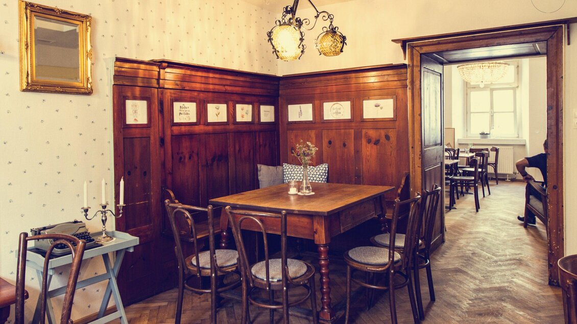 Ein einladendes Esszimmer mit einem Holzstisch und Stühlen. An den Wänden befinden sich dekorative Elemente und ein warmes Licht sorgt für eine gemütliche Atmosphäre. | © Cafe Fotter