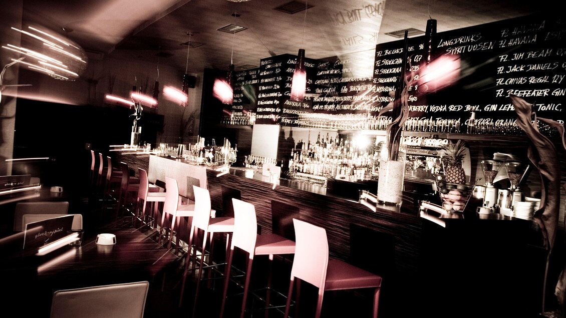 Ein eleganter Barbereich mit hohen Stühlen und einer langen Theke. Im Hintergrund sind die Getränkekarten an der Wand sichtbar. | © Cafe Glockenspiel