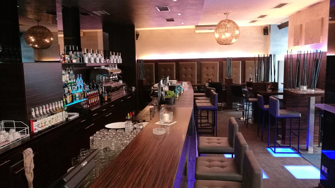 Eine stilvolle Bar mit einer langen Holztheke und modernen Sitzgelegenheiten. Die Beleuchtung schafft eine elegante Atmosphäre. | © Cafe Glockenspiel