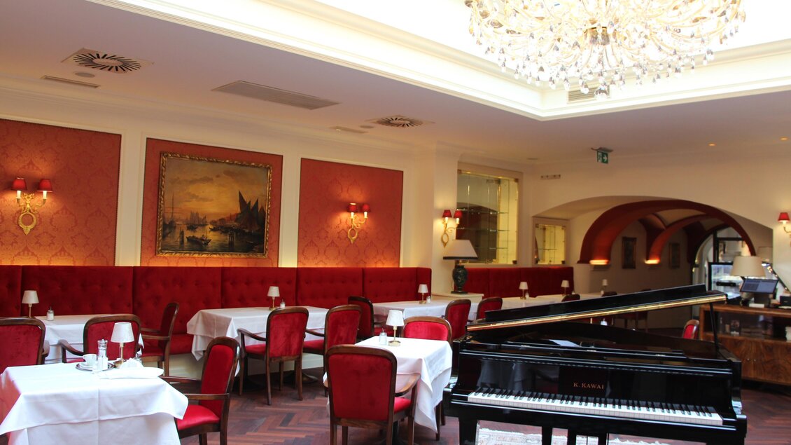 Innenraum mit roten Samtsesseln, weißen Tischdecken, großem Kronleuchter und schwarzem Flügel in klassisch-edler Café-Atmosphäre | © Region Graz - Vanessa Züttl
