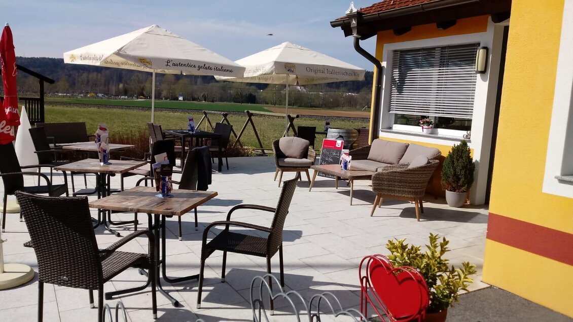 Ein gemütlicher Außenbereich mit Tischen und Stühlen sowie Sonnenschirmen. Die Umgebung ist grün und sonnig, ideal für entspannte Momente im Freien. | © Cafe Idylle