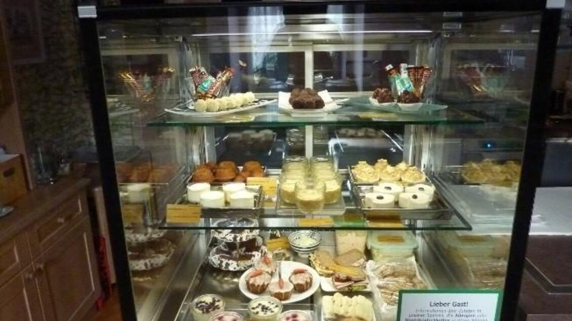 Eine Glasvitrine voller leckerer Desserts und Süßigkeiten. Verschiedene Kuchen, Torten und Häppchen sind schön angerichtet und ansprechend präsentiert. | © Cafe Katzengarten