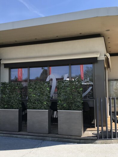 Ein modernes Café mit großen Fenstern und einem einladenden Eingang. Grünpflanzen umgeben die Terrasse und ein Schild weist auf Lieferdienste hin. | © Tourismusverband Oststeiermark