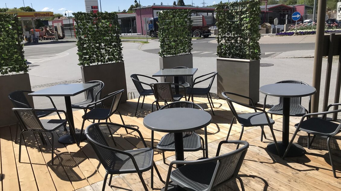 Ein Außenbereich mit Tischen und Stühlen auf einer Holzterrasse. Grüne Pflanzen bieten eine angenehme Atmosphäre. | © Tourismusverband Oststeiermark