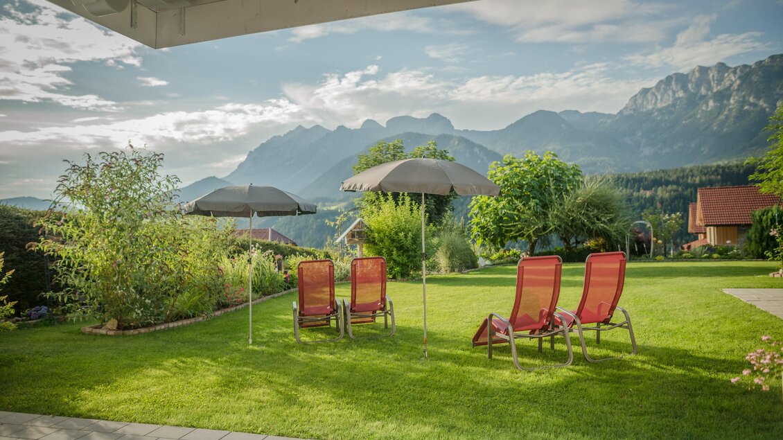 Ein schöner Garten mit Liegestühlen und Sonnenschirmen, umgeben von Bergen. Die Landschaft ist grün und einladend, ideal zum Entspannen. | © Christine Höflehner