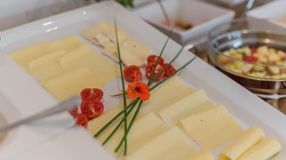 Ein großzügiges Teller mit verschiedenen Käsesorten, garniert mit frischen Kräutern und kleinen Tomaten. Im Hintergrund sind weitere Speisen in Schalen zu sehen. | © Christine Höflehner