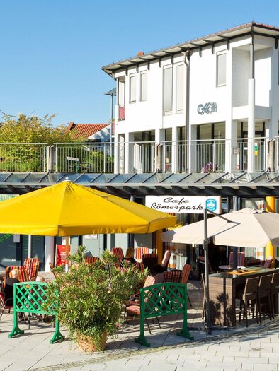 Eine sonnige Terrasse mit Stühlen und Schirmen. Im Hintergrund ist ein modernes Gebäude mit Bäumen zu sehen. | © TV Region Graz - René Vidalli