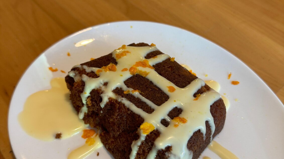 Ein Stück Schokoladenkuchen mit einer cremigen Vanillesoße. Der Kuchen ist dekoriert mit einem orangefarbenen Topping. | © Café Restaurant Freischwimmer