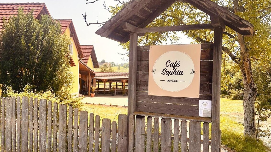 Ein einladendes Café mit einem Schild, das "Café Sophia" zeigt. Umgeben von Bäumen und einer grünen Wiese. | © Café Sophia