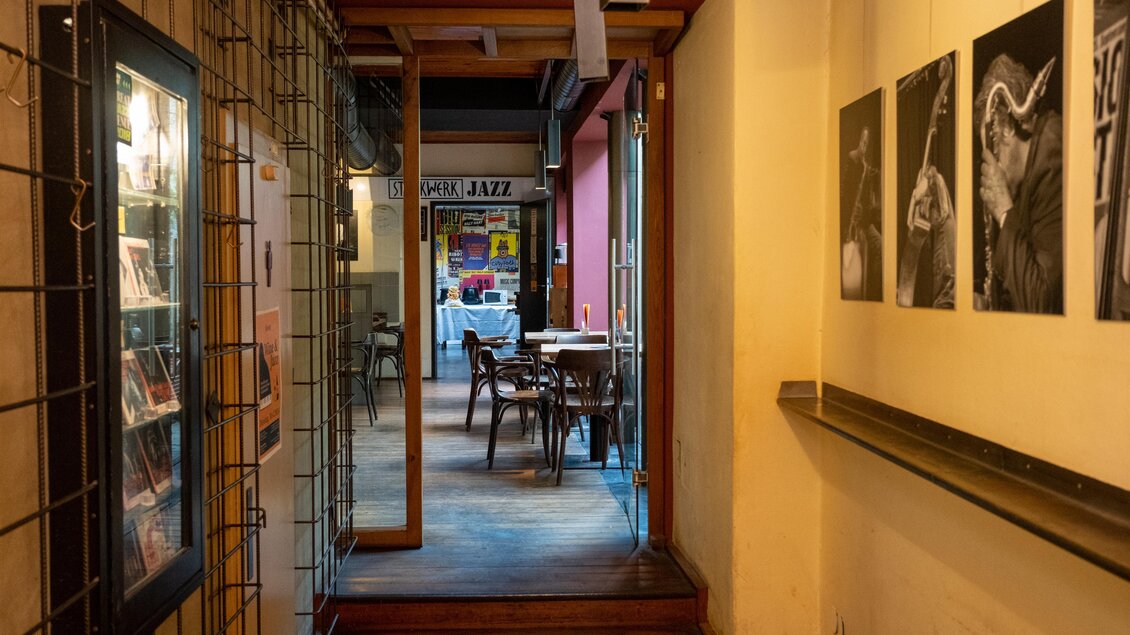 Ein einladender Flur mit Holzboden und Fotos an der Wand. Am Ende des Flurs ist ein Tisch mit Stühlen in einem gemütlichen Raum. | © Cafe Stockwerk - N.Popp