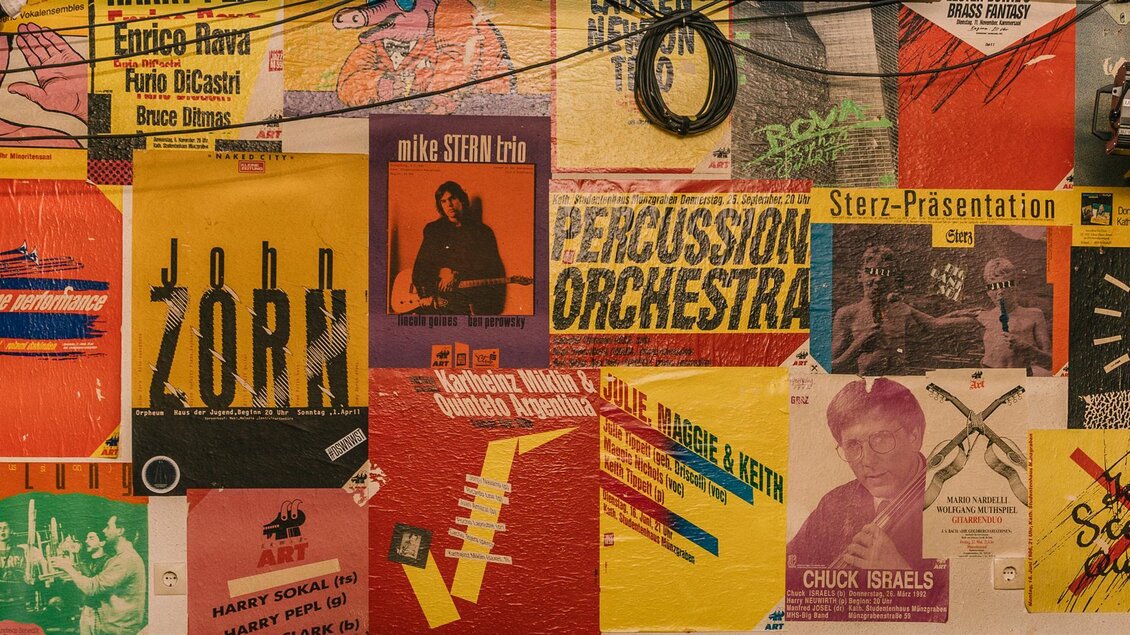 Eine bunte Wand mit verschiedenen Plakaten in vielen Farben. Die Plakate zeigen unterschiedliche Designs und Texte. | © Cafe Stockwerk - N.Popp