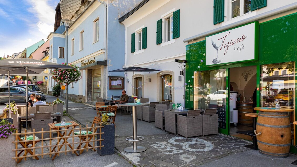 Straßenszene mit Außenbereich des Café Tiziano in Semriach, Tische, Sonnenschirme und Gäste bei Kaffee | © TV Region Graz - Harry Schiffer