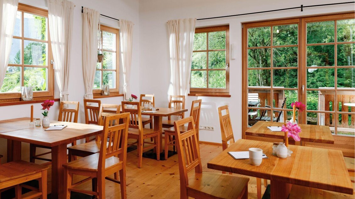 Ein helles und einladendes Café mit Holztischen und Stühlen. Große Fenster bieten einen Blick ins Grüne. | © Viola im Garten