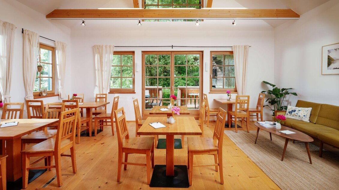 Ein helles und einladendes Café mit Holztischen und Stühlen. Große Fenster bieten einen Blick auf die Natur und lassen viel Tageslicht herein. | © Viola im Garten