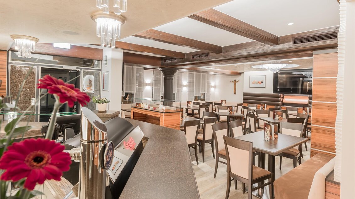 Ein modernes Restaurant mit eleganten Holzelementen und stilvollen Tischen. Im Vordergrund ist eine Bar mit blühenden Blumen zu sehen. | © Konditorei Regner