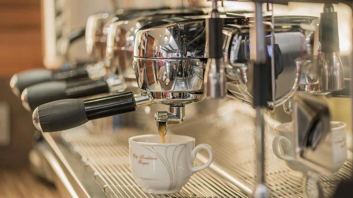 Eine Kaffeemaschine brüht gerade frischen Kaffee in eine weiße Tasse. Der glänzende Edelstahl und die Tasse sorgen für ein ansprechendes Bild. | © Konditorei Regner