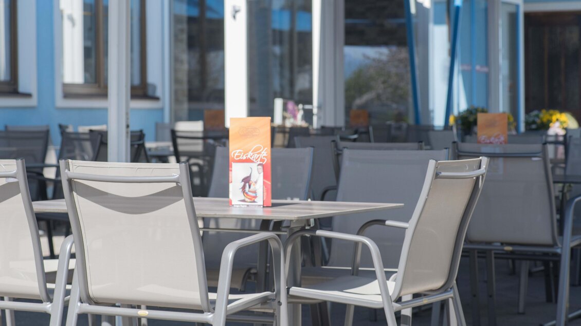 Ein gemütlicher Außenbereich mit leeren Tischen und Stühlen. Auf einem Tisch liegt ein Menü. | © Konditorei Regner