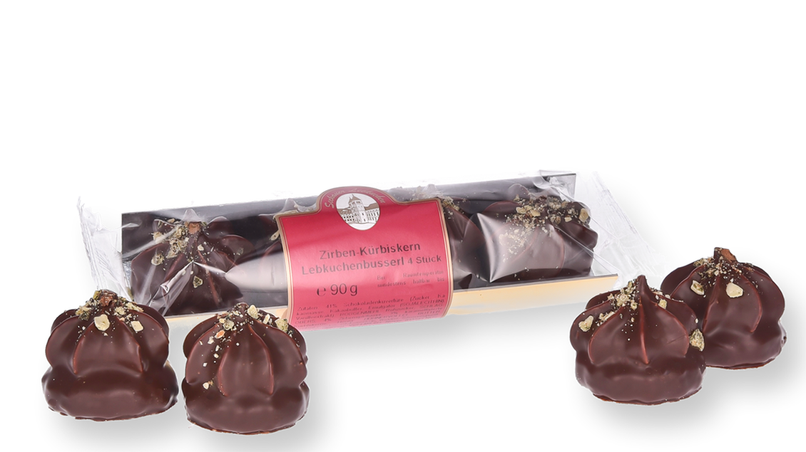 Eine Packung mit Schokoladenkugeln liegt neben vier weiteren, ebenfalls in Schokolade gehüllten Pralinen. Die Pralinen sind mit Nüssen dekoriert und haben eine glatte Oberfläche. | © Konditorei Regner