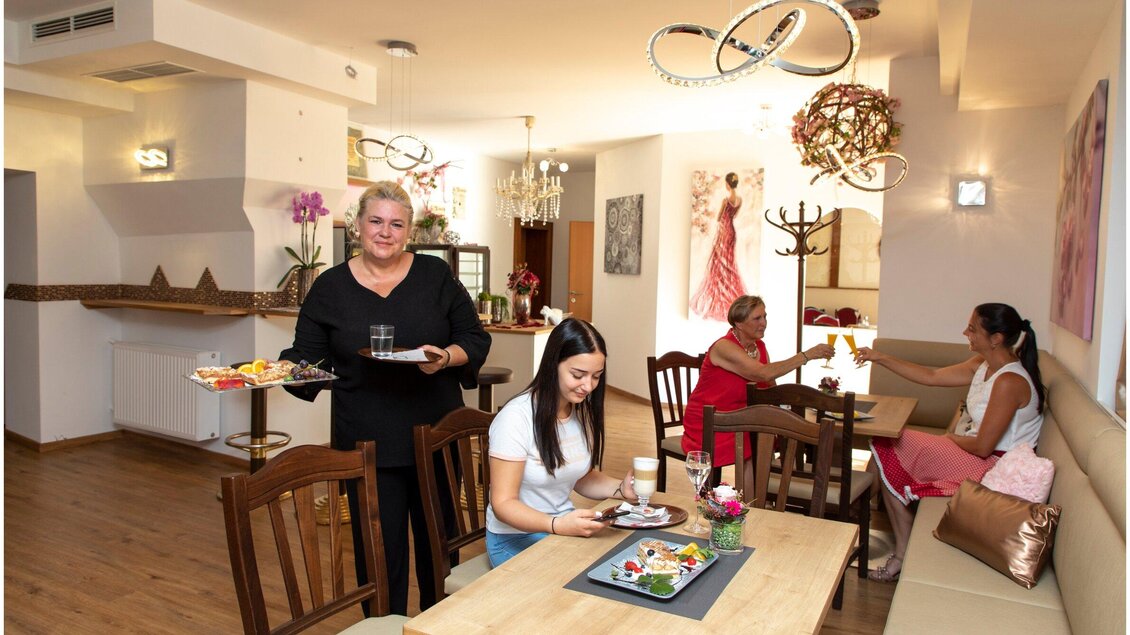 Ein gemütliches Restaurant mit mehreren Gästen. Eine Kellnerin serviert Essen, während andere Gäste an einem Tisch entspannen. | © TV Region Graz - J. Lunghammer