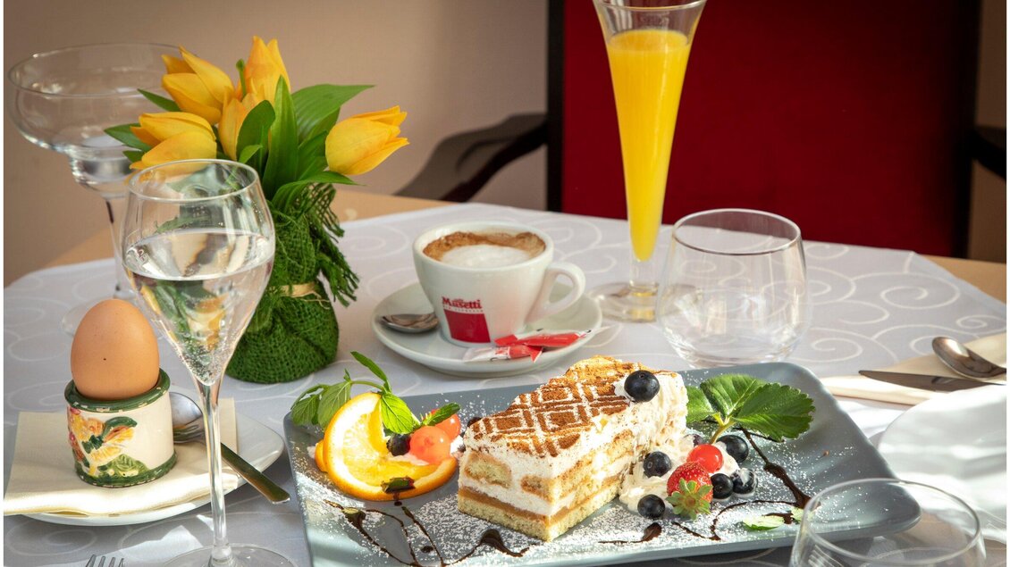 Ein gedeckter Tisch mit einem Dessert, einer Tasse Kaffee und einem Glas Getränk. Auf dem Tisch sind auch frische Blumen und eine aufwendige Dekoration. | © TV Region Graz - J. Lunghammer