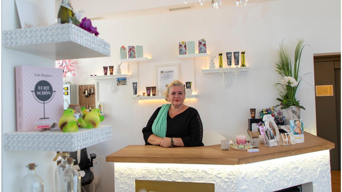 Ein einladender Salon mit einer freundlichen Mitarbeiterin am Empfang. Im Hintergrund befinden sich Produkte auf Regalen und eine dekorative Pflanzenanordnung. | © TV Region Graz - J. Lunghammer