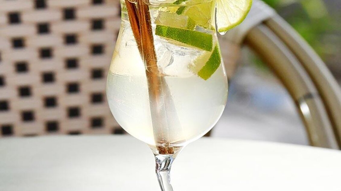 Ein erfrischender Cocktail in einem eleganten Glas mit Limetten und Minze. Er steht auf einem Holzuntersetzer und ist perfekt für einen entspannten Tag. | © Cafe Barletti