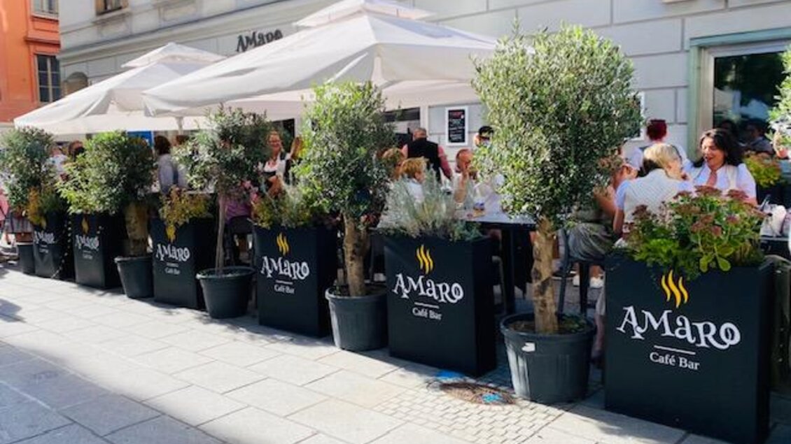 Ein gemütliches Café mit Schirmen und Pflanzen im Freien. Viele Menschen genießen ihre Zeit auf der Terrasse. | © Amaro