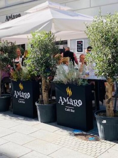 A cozy café with umbrellas and plants outside. Many people enjoy their time on the terrace. | © Amaro