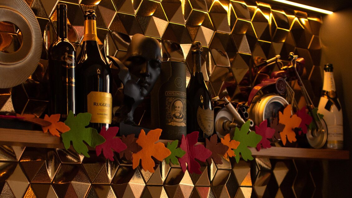 Eine stilvolle Bar mit verschiedenen Flaschen und einer dekorativen Holzablage. Bunte Blätter verleihen dem Ambiente eine gemütliche Atmosphäre. | © Amaro