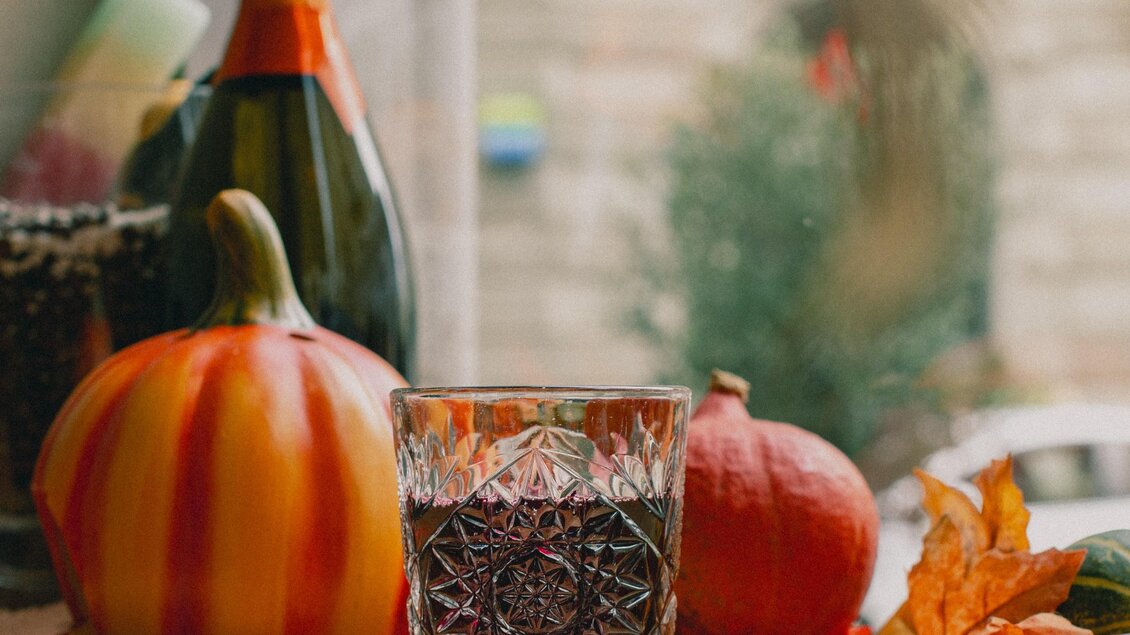Ein schöner Tisch mit Kürbissen, einem Trinkglas und einer Sektflasche. Im Hintergrund sind herbstliche Blätter zu sehen. | © Amaro