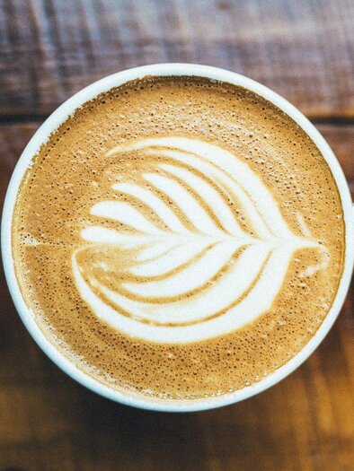 A cup of latte macchiato with a beautiful leaf pattern made from milk foam. It is resting on a wooden surface. | © Erlebnisregion Murtal