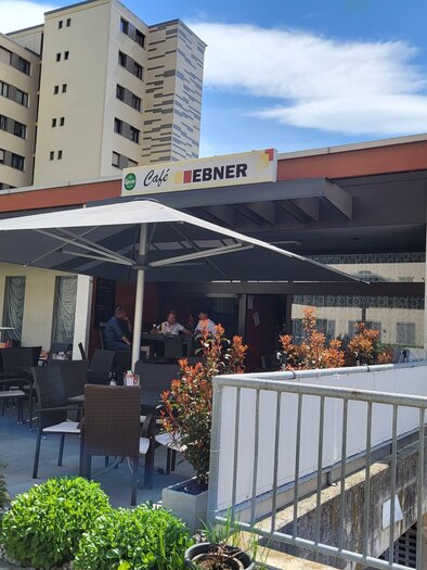 A café with a covered outdoor area and seating. In the background, several residential buildings are visible. | © TV Hochsteiermark