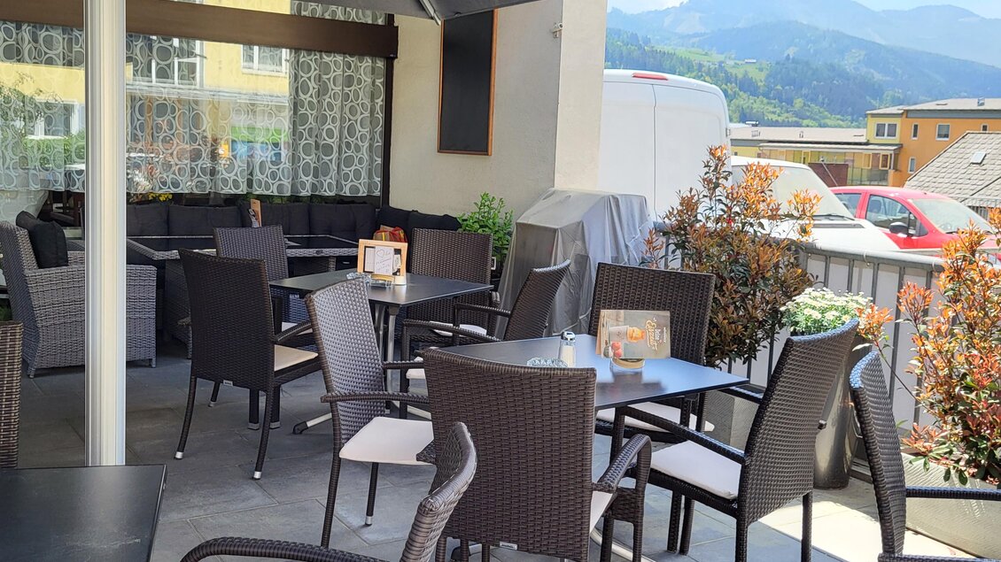 Eine gemütliche Terrasse mit Rattanmöbeln und hübschen Pflanzen. Im Hintergrund sind Berge und ein klarer Himmel zu sehen. | © TV Hochsteiermark
