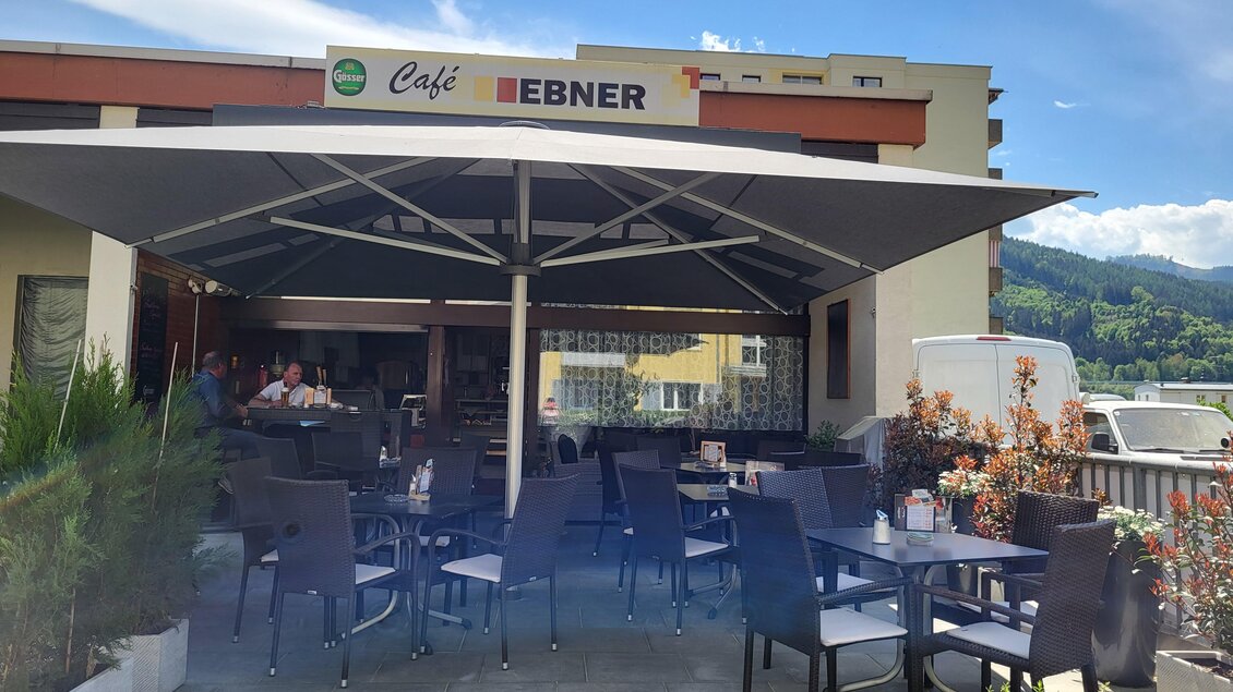 Ein einladendes Café mit Terrassenmöbeln unter einem großen Sonnenschirm. Im Hintergrund sind eine gemütliche Atmosphäre und eine schöne Aussicht zu sehen. | © TV Hochsteiermark