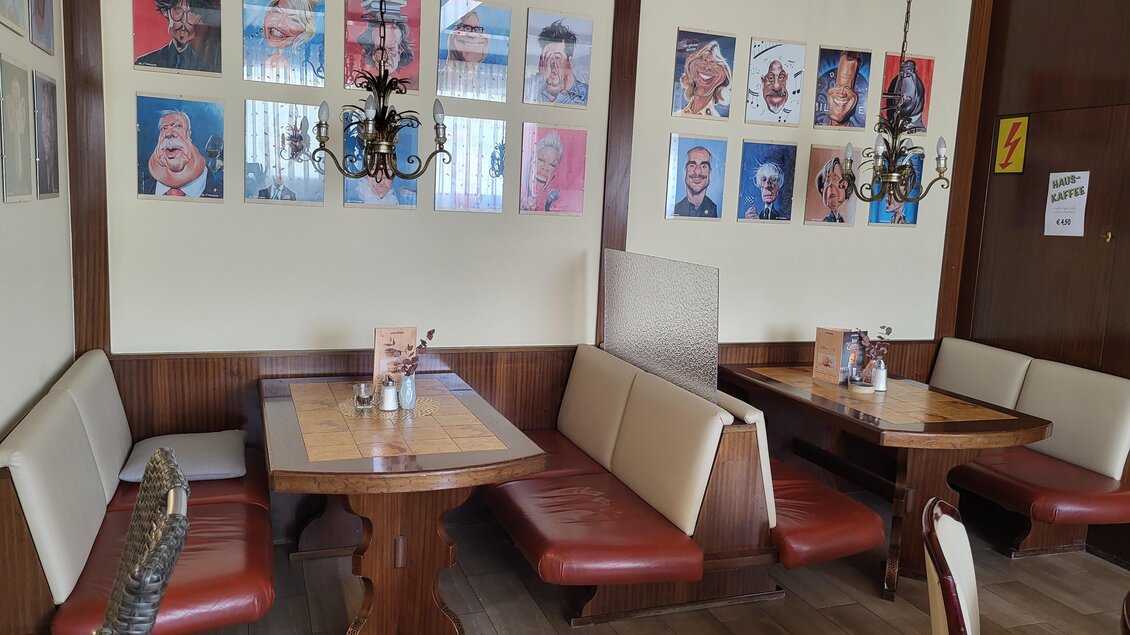 Ein gemütliches Restaurant mit Holz-Tischen und roten Polstermöbeln. An der Wand hängen bunte Bilder von verschiedenen Personen. | © TV Hochsteiermark