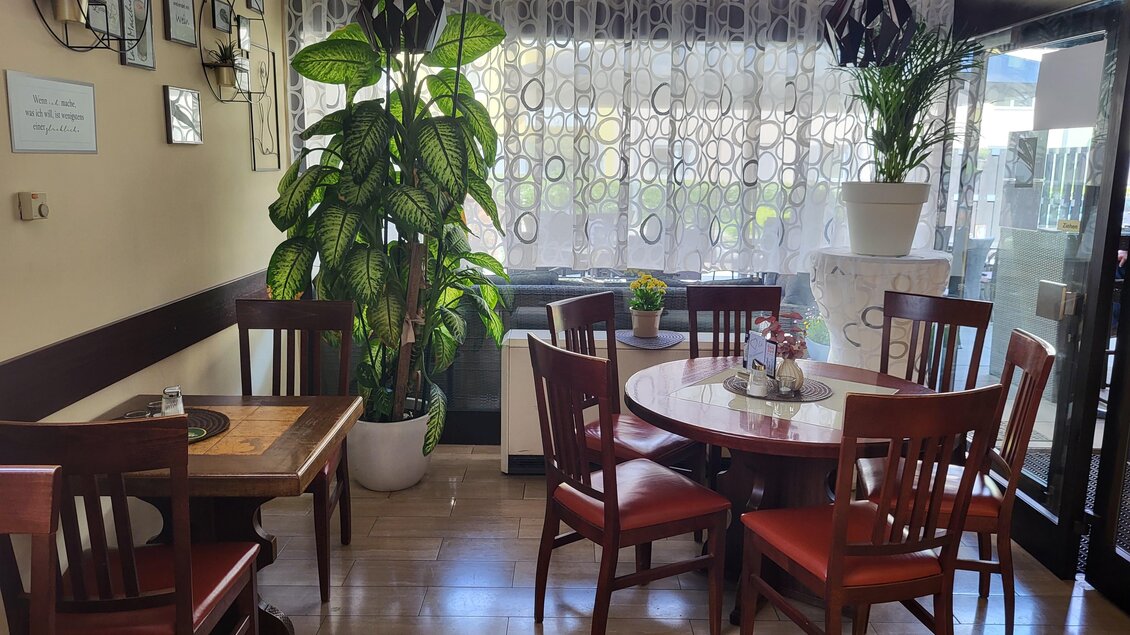 Ein gemütlicher Essbereich mit Holztischen und -stühlen. Große Fenster mit Vorhängen und Pflanzen sorgen für eine einladende Atmosphäre. | © TV Hochsteiermark