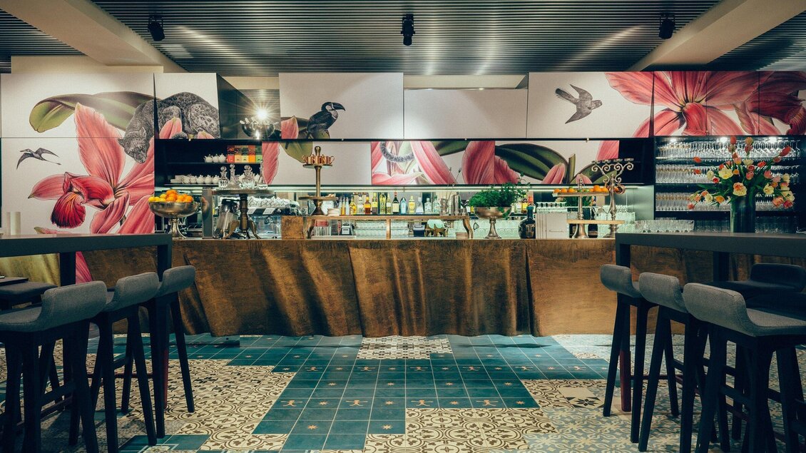 Eine elegante Bar mit modernen Möbeln und farbenfrohen Wandmalereien. Der Raum ist hell und einladend, ideal für gesellige Treffen. | © Cafe Promenade - Joel Kernasenko