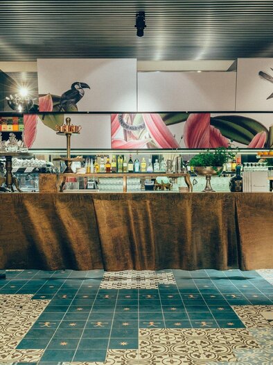 An elegant bar with modern furniture and colorful murals. The space is bright and inviting, perfect for social gatherings. | © Cafe Promenade - Joel Kernasenko