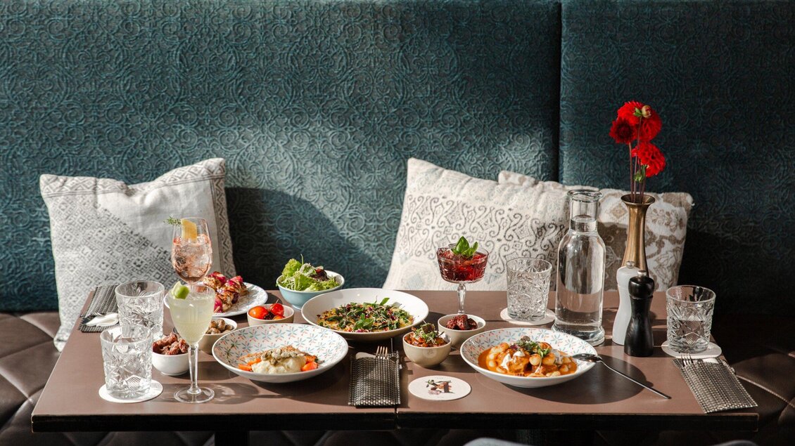 Ein schön gedeckter Tisch mit verschiedenen Gerichten, Getränken und Dekoration. Im Hintergrund sind gemütliche Kissen zu sehen. | © Cafe Promenade - Bobbys Agency