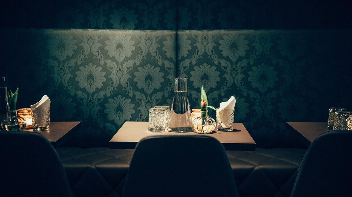 Ein stilvolles Restaurant mit gedämpftem Licht. Auf den Tischen stehen Gläser und Kerzen, um eine gemütliche Atmosphäre zu schaffen. | © Cafe Promenade - Joel Kernasenko