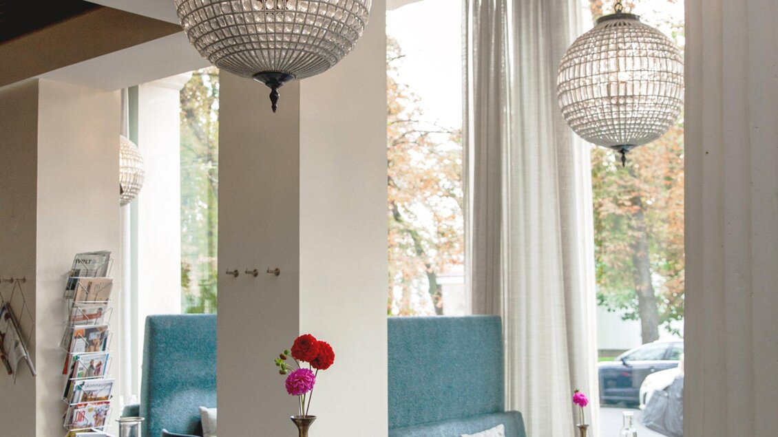 Ein stilvolles Café mit gemütlichen Sitzgelegenheiten und modernen Lampen. Große Fenster lassen viel Tageslicht herein und schaffen eine einladende Atmosphäre. | © Cafe Promenade - Bobbys Agency