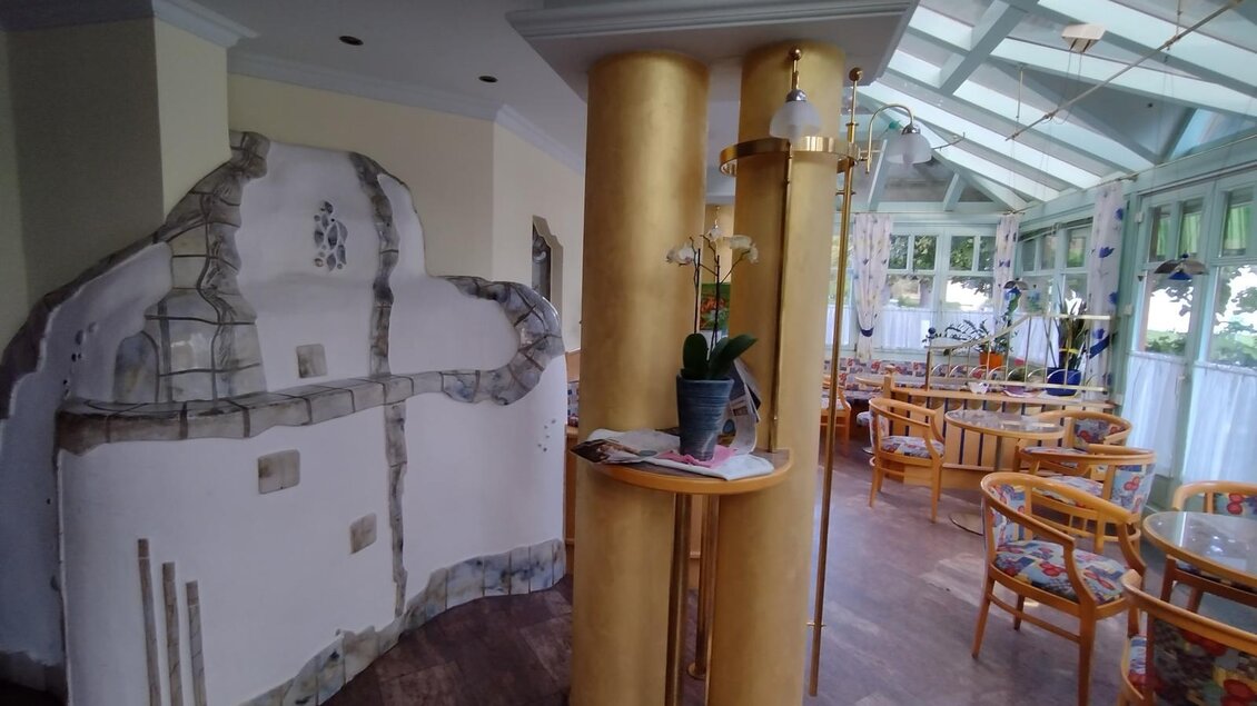 Ein elegantes Restaurant mit einem modernen Innenraum und einer warmen Farbauswahl. Im Vordergrund steht eine dekorative Säule und der Raum ist mit Tischen und Stühlen ausgestattet.