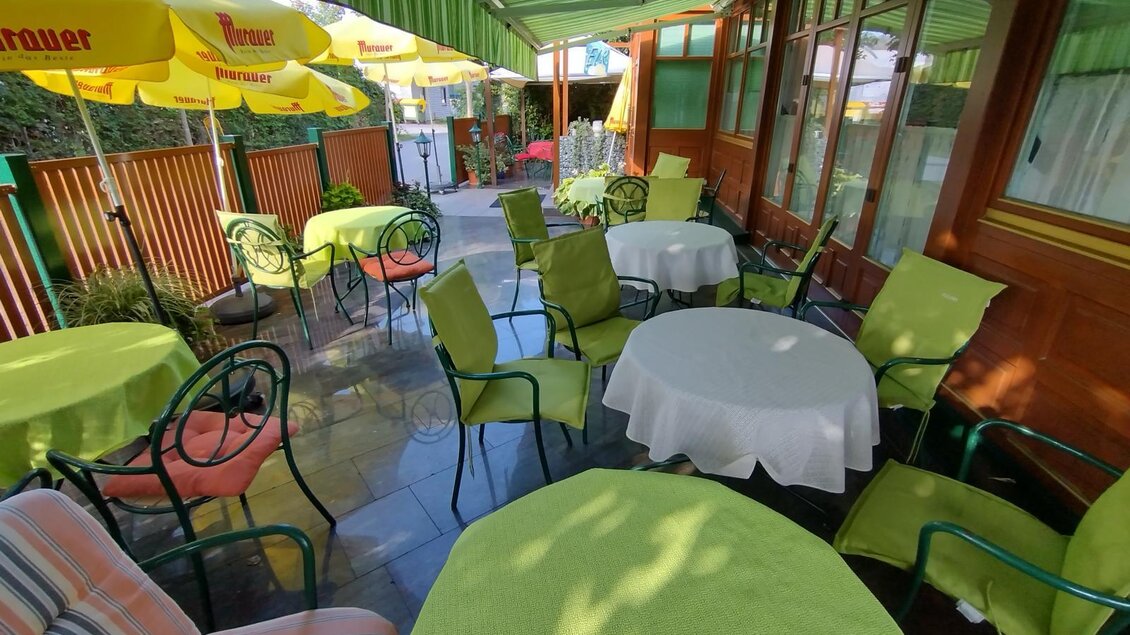 Ein einladender Außenbereich mit runden Tischen und Stühlen, alles in leuchtenden Grüntönen. Sonnenschirme bieten Schatten und eine entspannte Atmosphäre.