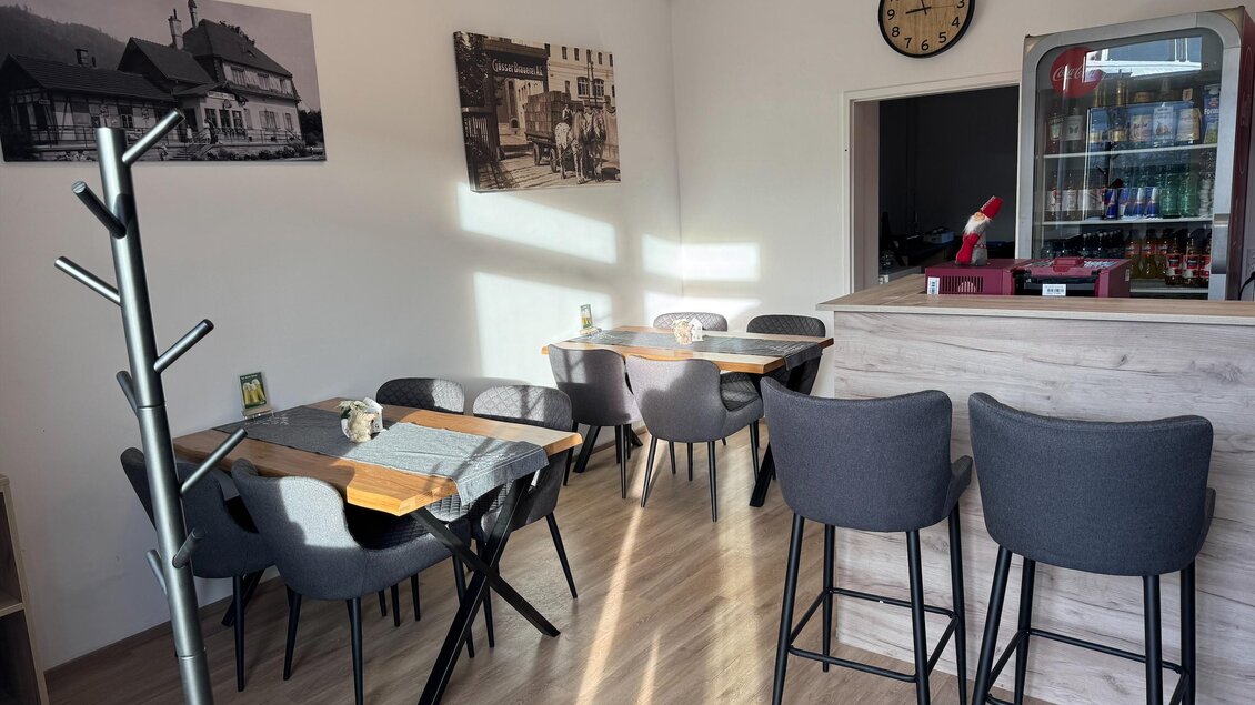 Ein gemütliches Café mit Holzstühlen und Tischen. An der Wand hängen historische Fotos und eine Uhr zeigt die Zeit an. | © SV Hinterberg
